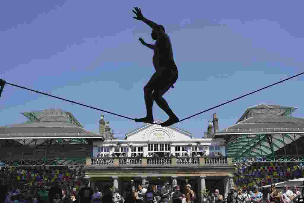 A performer walks on a tightrope at Covent Garden during a sunny day in London.