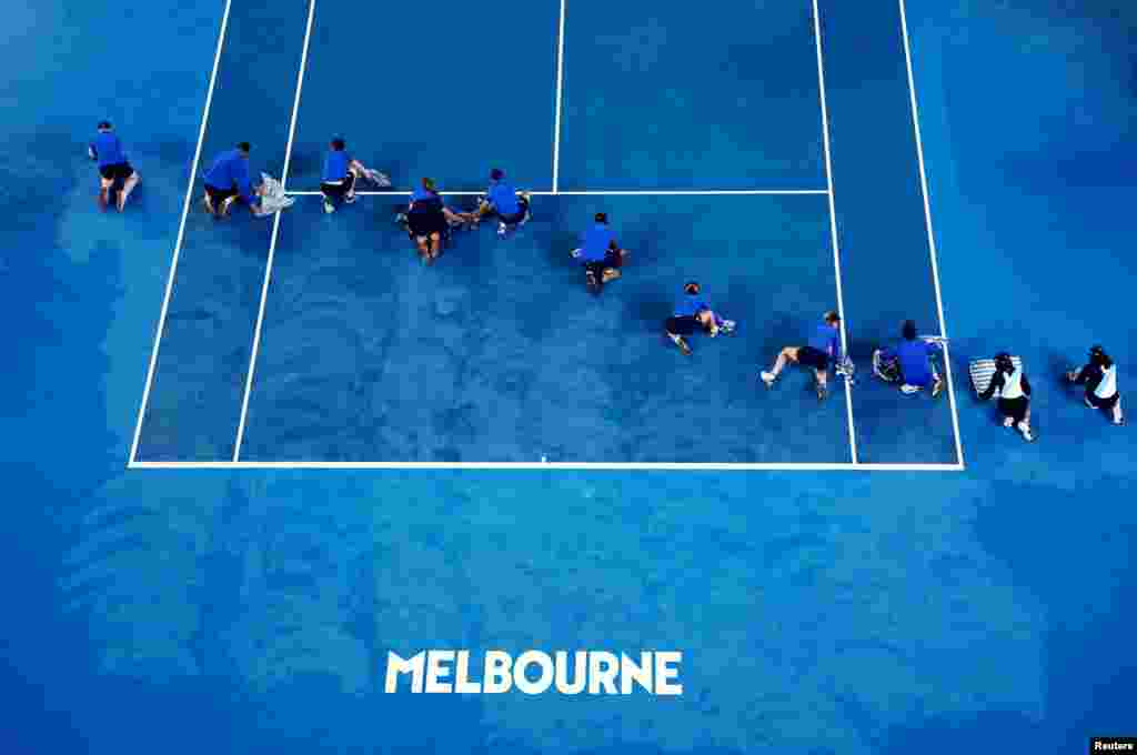 Ground staff members dry the court during the second round match of the Australian Open tennis championships between Poland's Iga Swiatek and Danielle Collins of the U.S. as the match is interrupted due to rain in Melbourne, Australia.