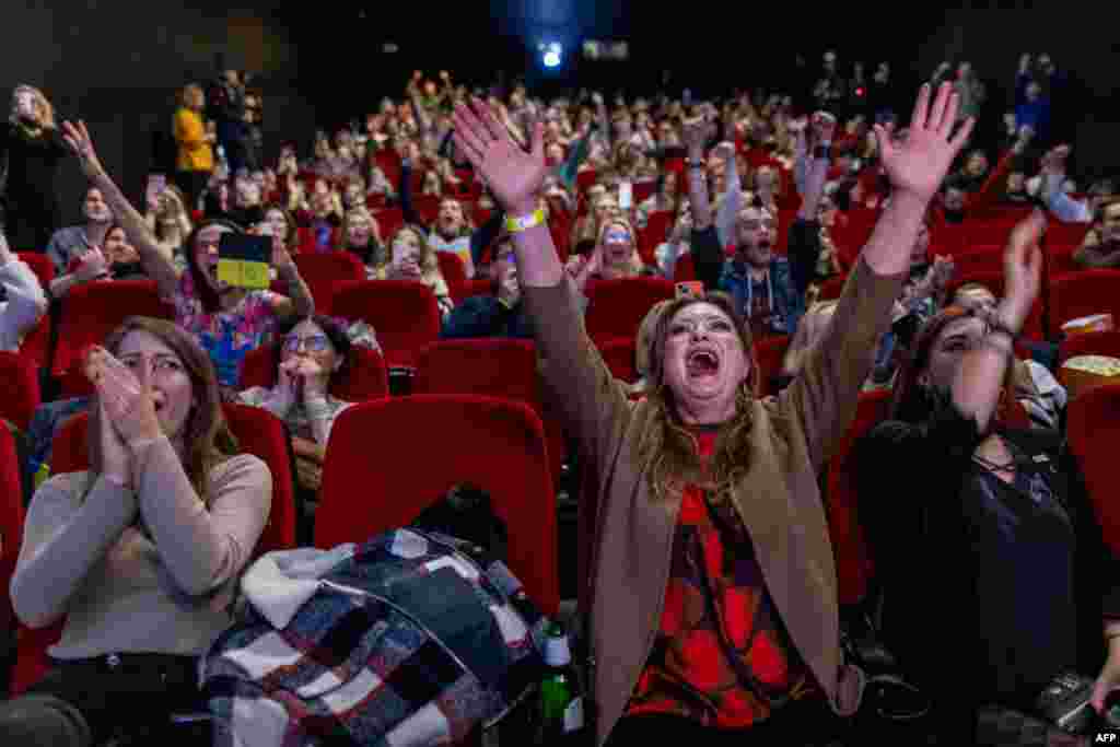 People react as they watch a parliament session on a confidence vote of outgoing Polish prime minister Mateusz Morawiecki, in a cinema in Warsaw. 