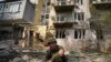 Ukrajinski vojnik prikuplja ostatke municije posle ruskog napada u kojem su oštećene zgrade u Harkovu (Foto: AP/Andrii Marienko)