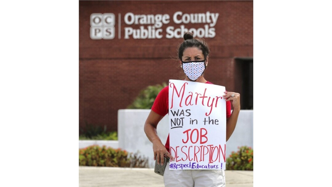 FILE - In this Tuesday, July 7, 2020 file photo, Rachel Bardes holds a sign in front of the Orange County Public Schools headquarters as teachers protest with a car parade in Orlando, Fla. (Joe Burbank/Orlando Sentinel via AP, File)