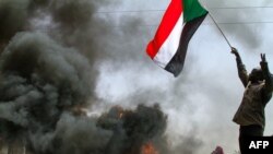 Mwanamume akipeperusha bendera ya taifa karibu na matairi yanayowaka wakati wa maandamano katika mji Khartoum kupinga mapinduzi ya kijeshi, Machi 24, 2022. Picha na AFP.