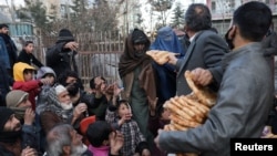 Seorang perempuan Afghanistan menerima bantuan sepotong roti di depan toko roti di antara kerumunan di Kabul, Afghanistan, 31 Januari 2022. (Foto: REUTERS/Ali Khara)