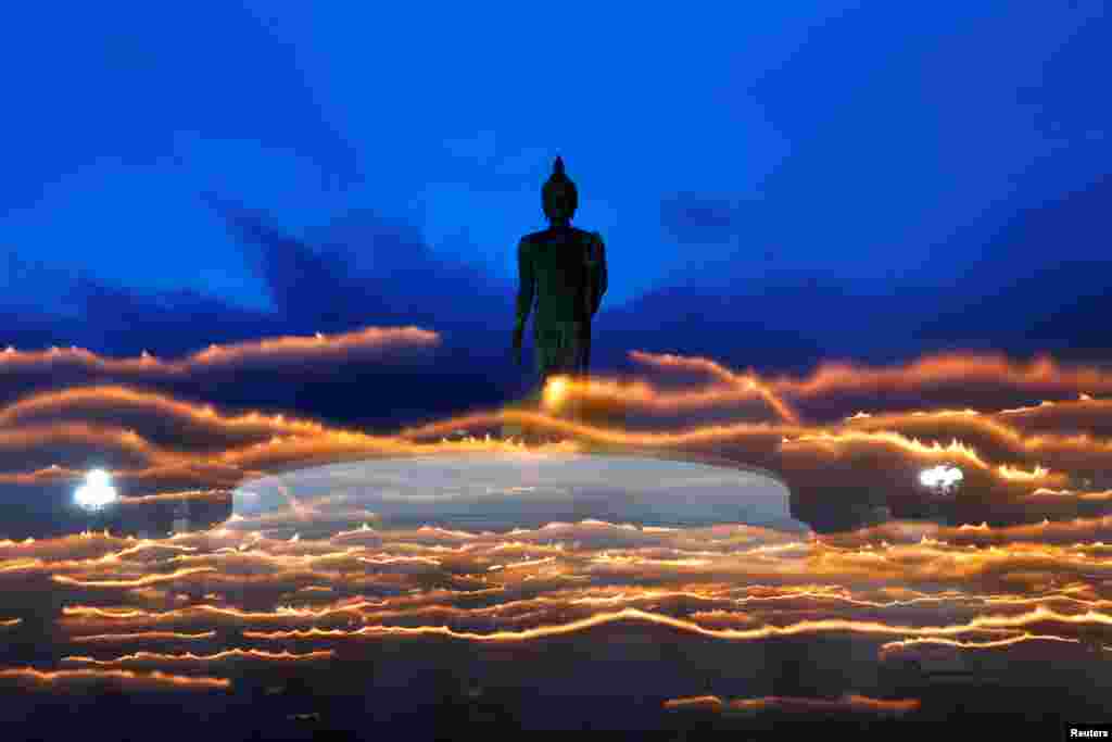 Warga Budha menyalakan lilin sambil mengelilingi patung Buddha raksasa pada festival Hari Asanha Puja, di candi Nakhon Pathom, pinggiran Bangkok, Thailand.