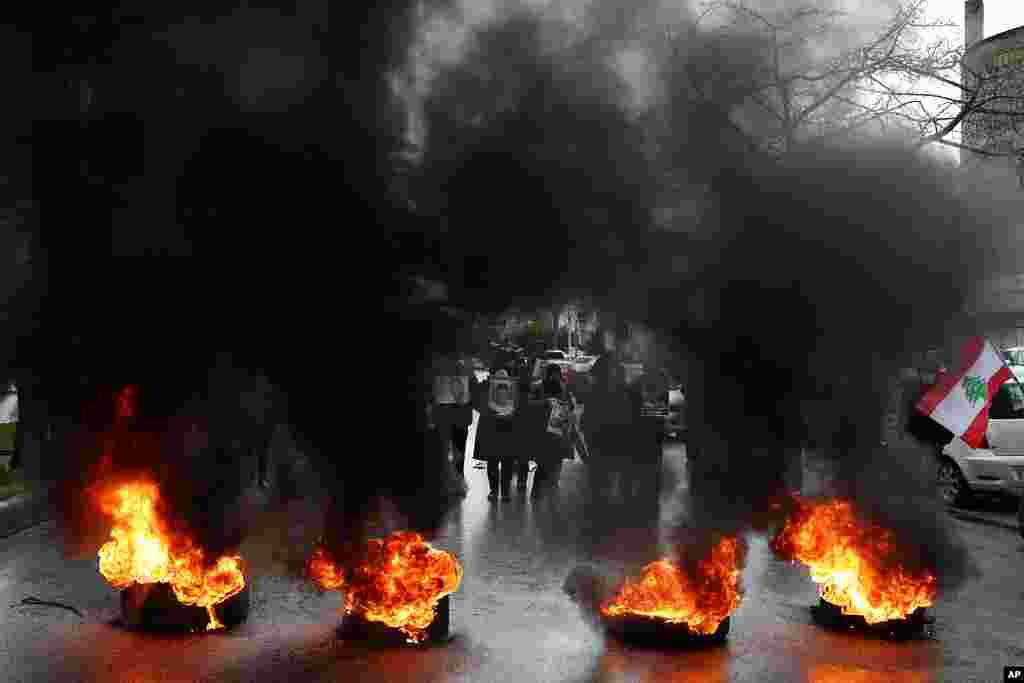 Relatives of victims of the Aug. 4, 2020, Beirut port explosion hold portraits of their loved one who killed during the explosion, as they burn tires to block a road during a sit-in outside the Justice Palace, in Beirut, Lebanon.