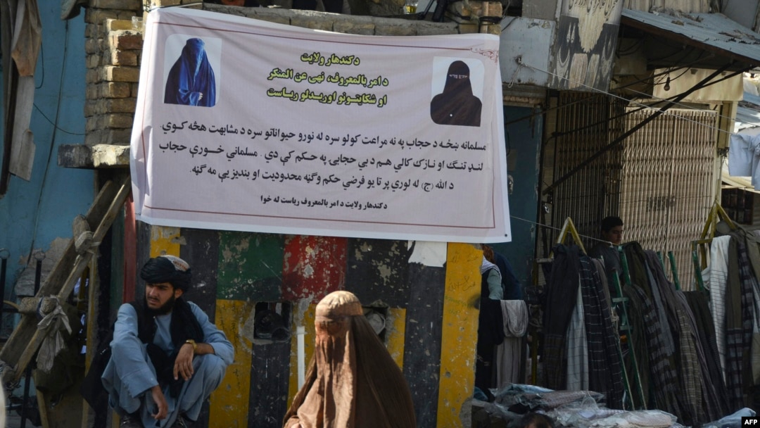 یک زن برقع‌پوش افغانستانی در حال عبور از مقابل پوستری که از زنان می‌خواهد حجاب داشته باشند. قندهار، ۱۶ ژوئن ٢٠٢٢