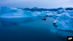 A boat navigates at night between icebergs in eastern Greenland, late Aug. 15, 2019.