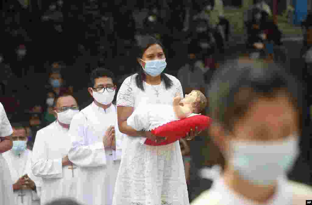 A woman, wearing face mask, carries baby Jesus statue, during a procession for a Christmas mass service at a church in Bali, Indonesia.