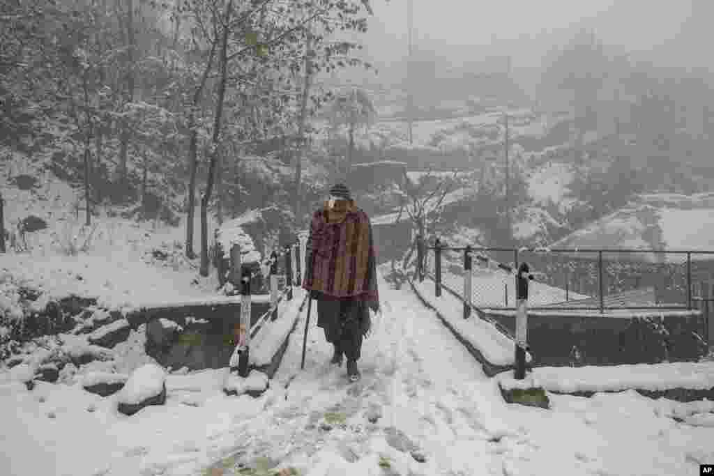 An elderly Kashmir villager walks on a snow covered road during the season's first snowfall on the outskirts of Srinagar, Indian-controlled Kashmir.
