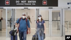 Mike Rustici, left, and Linda Scruggs exit customs after arriving on a flight from Lima, Peru, March 21, 2020, at Miami International Airport in Miami.