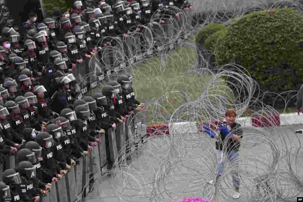 Riot police stand guard as a protester attempts to get through barbed wire barricading the base entrance of the 11th Infantry Regiment, a palace security unit under direct command of the Thai king, in Bangkok, Thailand.