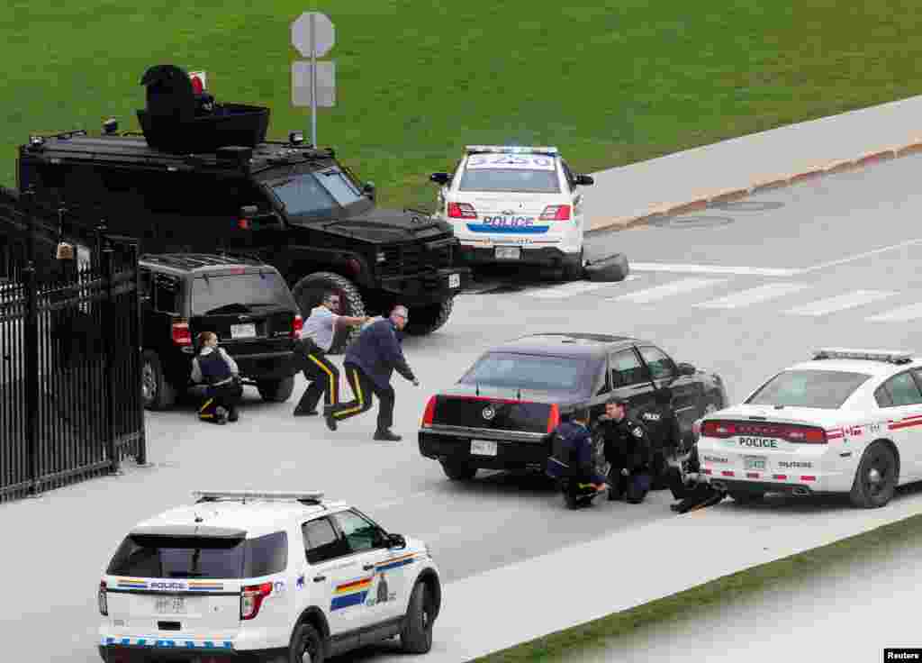 Nhân viên cảnh sát Canada núp sau xe cộ gần Tòa nhà Quốc hội ở Ottawa sau vụ nổ súng.