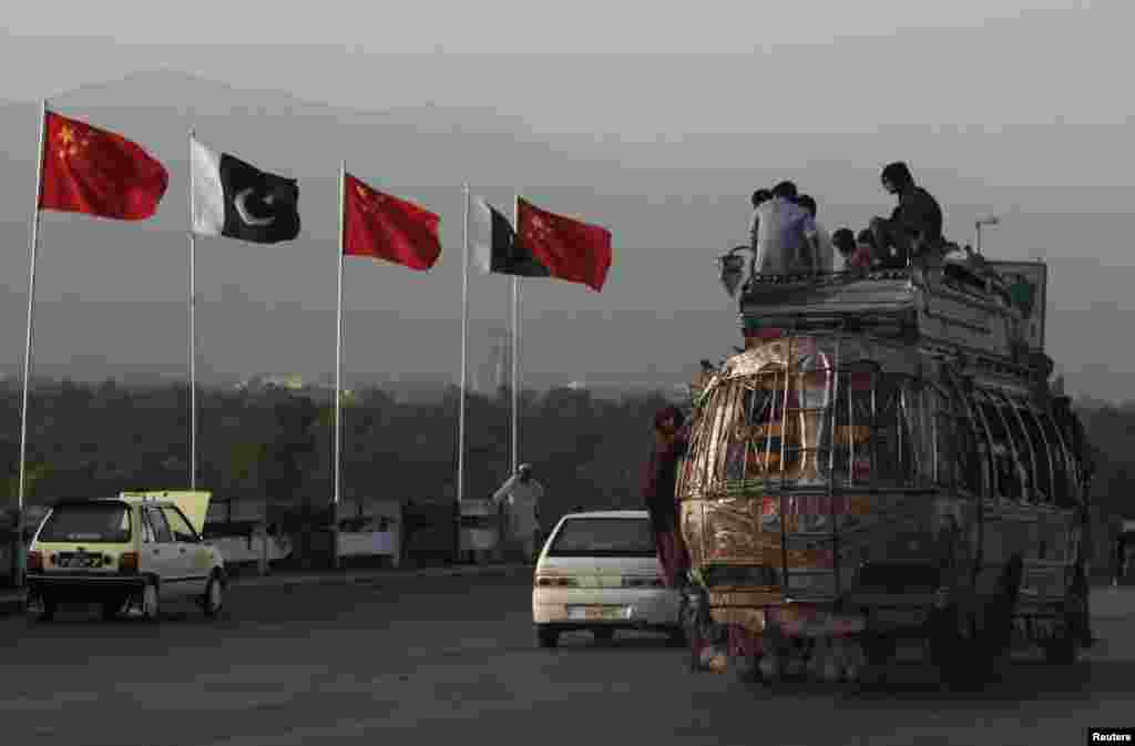 People sit on top of a bus as they go past flags of Pakistan and China that are displayed along a road, ahead of Chinese Premier Li Keqiang's visit to Islamabad.