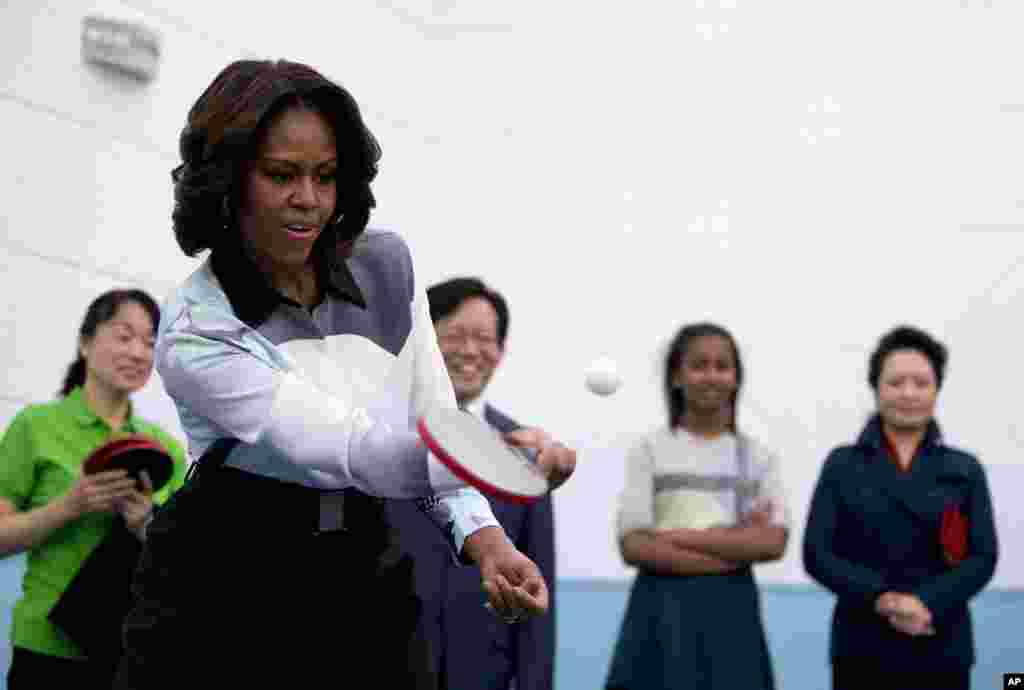 U.S. First Lady Michelle Obama plays table tennis as Peng Liyuan, wife of Chinese President Xi Jinping, right, and others watch her during their visit to the Beijing Normal School, a school that prepares students to attend colleges overseas in Beijing, China.