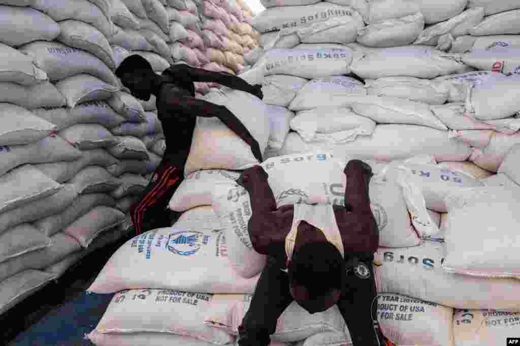 Sudanese local community members carry to deliver sacks of sorghum for Ethiopian refugees who fled the country's Tigray conflict, in a warehouse erected by the World Food Program (WFP) at Um Raquba refugee camp in Gedaref, eastern Sudan.