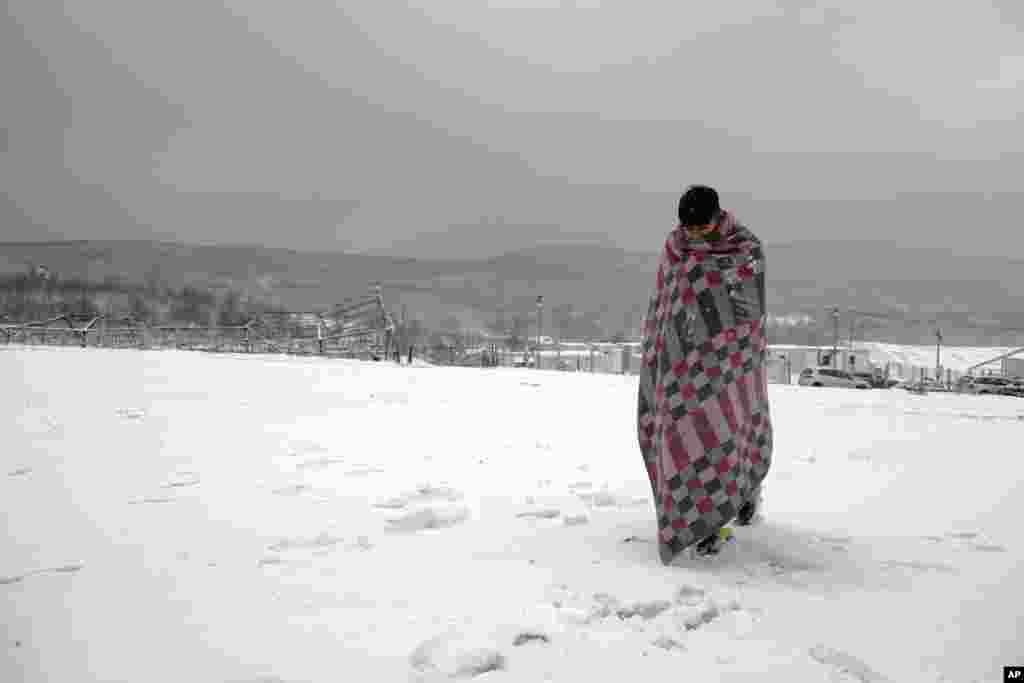 A migrant wrapped in a blanket, walks through the snow at the Lipa camp northwestern Bosnia, near the border with Croatia, Dec. 26, 2020.