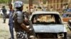 A policeman stands near damaged vehicles after a suicide car bomber killed five people on a street of popular bars and restaurants in Sabon Gari, Kano, Nigeria, May 19, 2014.