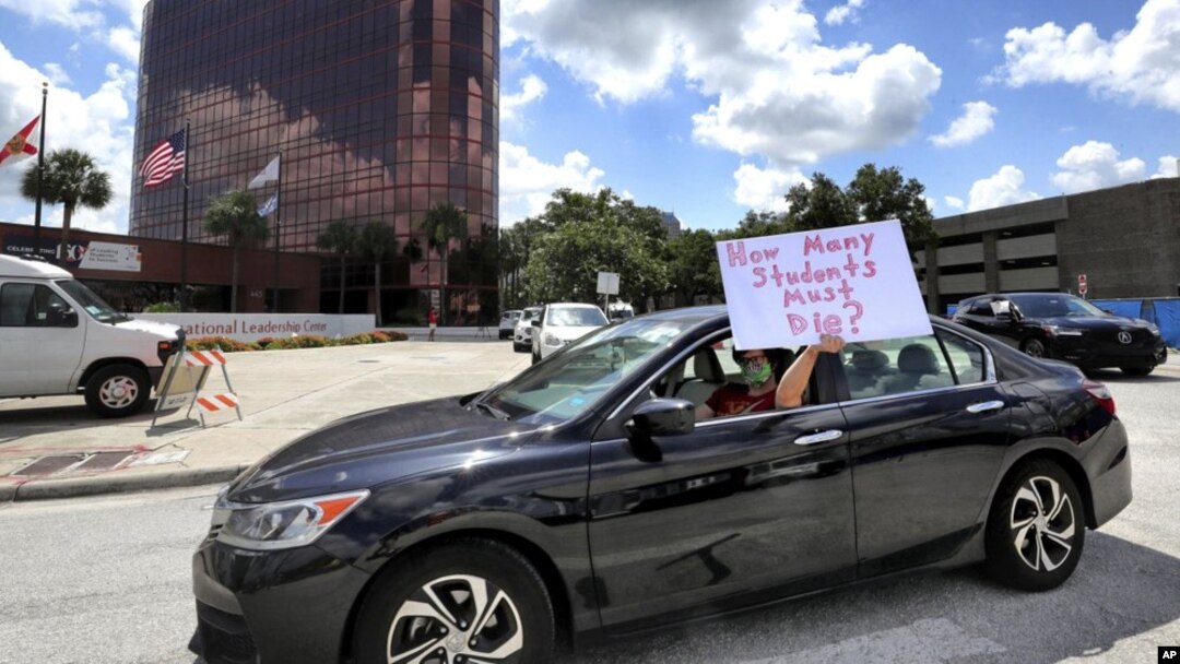 FILE - In this Tuesday, July 7, 2020 file photo, a teacher holds up a sign while driving by the Orange County Public Schools headquarters as educators protest in a car parade around the administration center in Orlando, Fla. (Joe Burbank/Orlando Sentinel via AP, File)