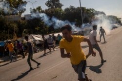 Refugees and migrants flee as tear gas is fired by riot police during clashes near the city of Mytilene on the Greek island of Lesbos, on September 12, 2020, a few days after a fire destroyed the Moria refugee camp.