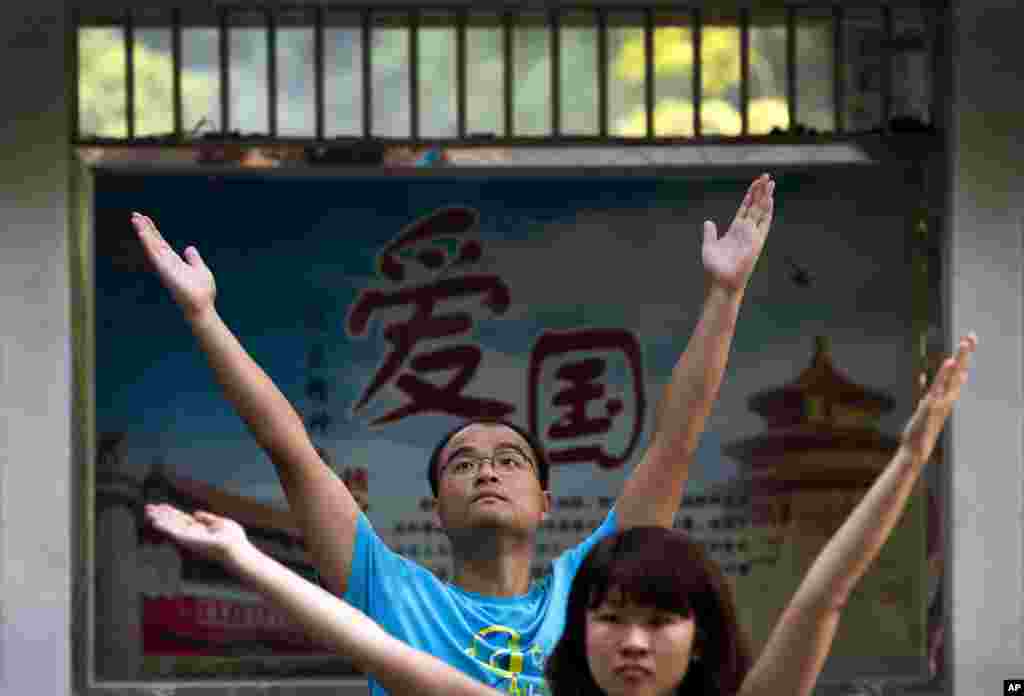 Employees of a Chinese bank take part in a motivation exercise at Ritan Park in Beijing. The word of a propaganda poster, background, reads "Patriotism."
