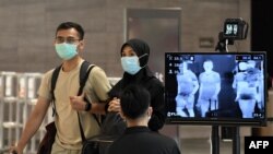 Sepasang suami istri, mengenakan masker di tengah kekhawatiran tentang penyebaran virus corona baru COVID-19, berjalan melewati pemeriksaan pemeriksaan suhu di Bandara Internasional Changi di Singapura, 27 Februari 2020. (Foto: AFP)