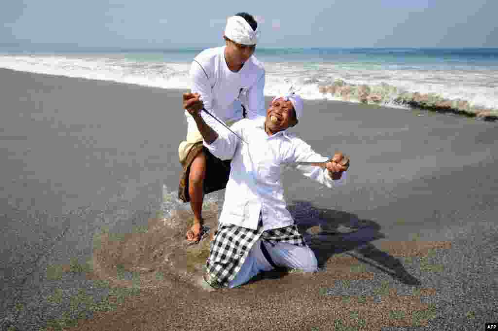 Seorang laki-laki Bali dalam keadaan trans menusuk dirinya dengan keris saat mengikuti upacara keagamaan Melasti di Pantai Petitenget di Kuta, Bali. Melasti adalah upacara penyucian yang diadakan beberapa hari sebelum Nyepi, hari Tahun Baru umat Hindu yang diperingati dengan keheningan, di mana umat Hindu di Pulau Bali tidak diperbolehkan untuk bekerja, bepergian atau bersenang-bersenang. 