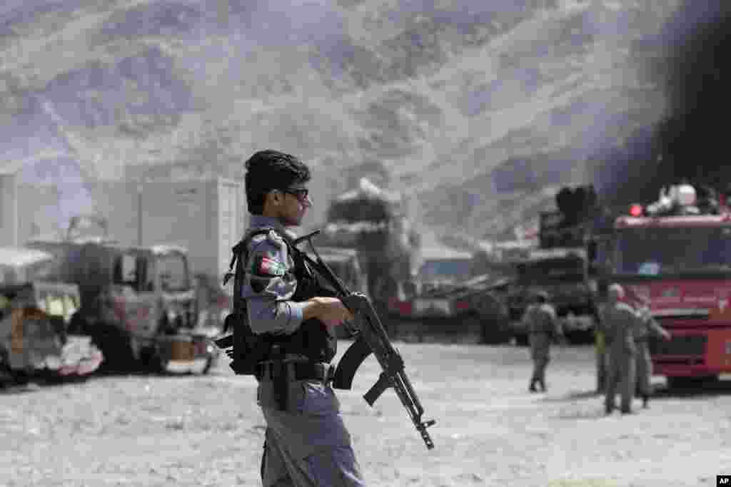 An Afghan police officer stands guard near burning NATO supply trucks following an attack by militants in Torkham, Afghanistan, Sept. 2, 2013.