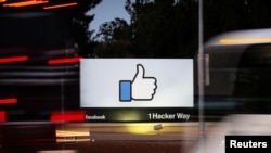 FILE - The entrance sign to Facebook headquarters is seen through two moving buses in Menlo Park, California, Oct. 10, 2018.