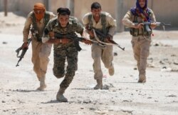 FILE - Kurdish fighters from the People's Protection Units (YPG) run across a street in Raqqa, Syria, July 3, 2017.