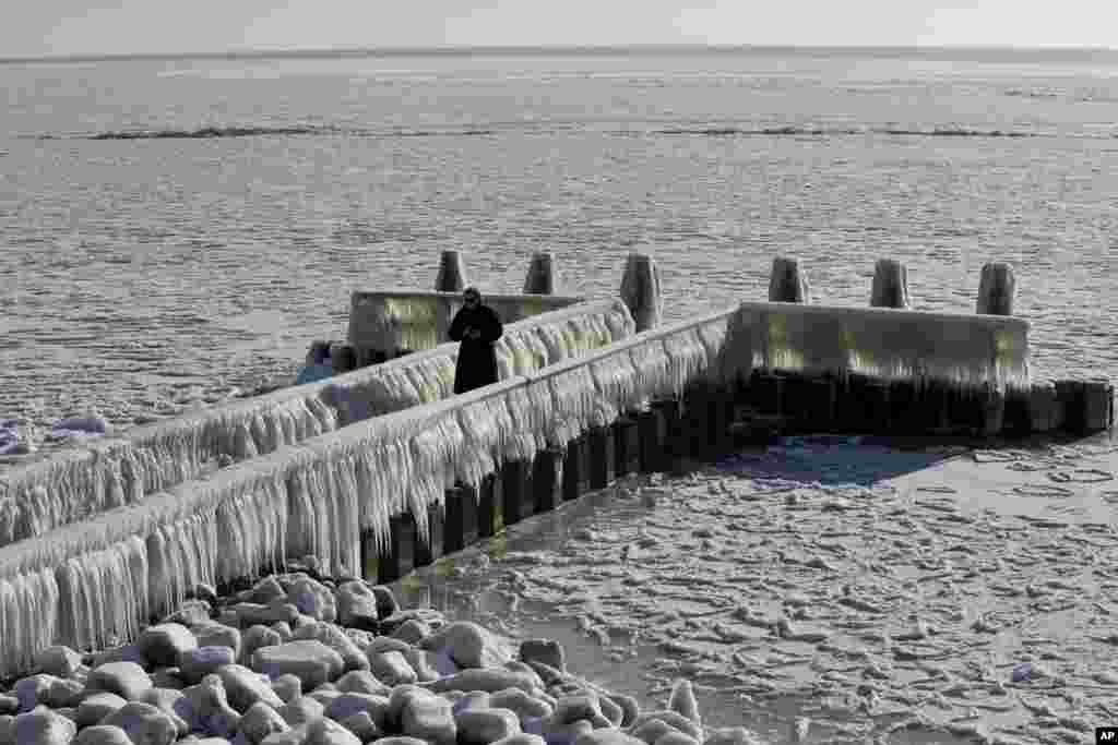 A woman takes pictures of icicles on a jetty at the Afsluitdijk, a dike separating IJsselmeer inland sea, and the Wadden Sea, Netherlands.