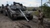 Припадник на украинската армија поминува покрај нефункционален руски тенк во градот Изјум