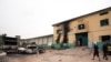 People walk past burned vehicles in front of a prison in Owerri, Nigeria, April 5, 2021, after hundreds of inmates escaped from the facility.