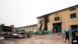 People walk past burned vehicles in front of a prison in Owerri, Nigeria, April 5, 2021, after hundreds of inmates escaped from the facility.