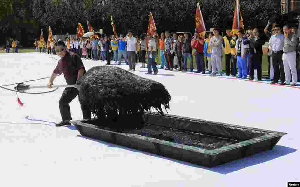Seniman Kaligrafi Zhang Kesi mencelupkan kuasnya ke dalam tinta saat ia mengerjakan kaligrafi raksasa di Shenyang, Provinsi Liaoning, China. Zhang, terkenal karena karya-karya kaligrafi tulisan China raksasa yang ditulis menggunakan kuas berukuran besar, menyelesaikan karya terbarunya. Karya itu akan disajikan sebagai hadiah untuk Acara Pertandingan Olahraga Nasional mendatang yang akan diselenggarakan di kota itu dari tanggal 31 Agustus hingga 12 September.