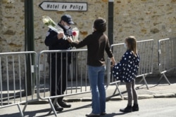 A woman hands flowers to an officer to be taken to the police station where a female police worker was stabbed to death two days earlier, in Rambouillet, southwest of Paris, France, April 25, 2021.
