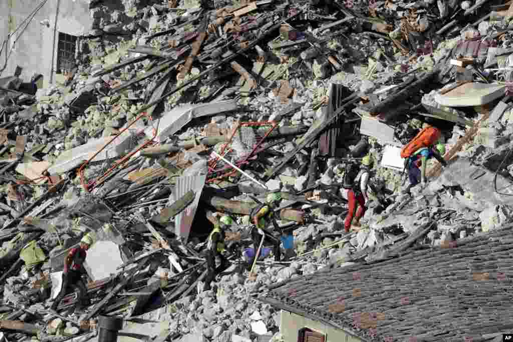 Petugas penyelamatan melewati rumah-rumah yang hancur akibat gempa di Pescara Del Tronto, Italia tengah (25/8). (AP/Gregorio Borgia)
