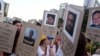 ARCHIVO - Manifestantes sostienen carteles de cartón que muestran imágenes de familiares y amigos asesinados durante protestas antigubernamentales, en Caracas, Venezuela, el 18 de marzo de 2014.