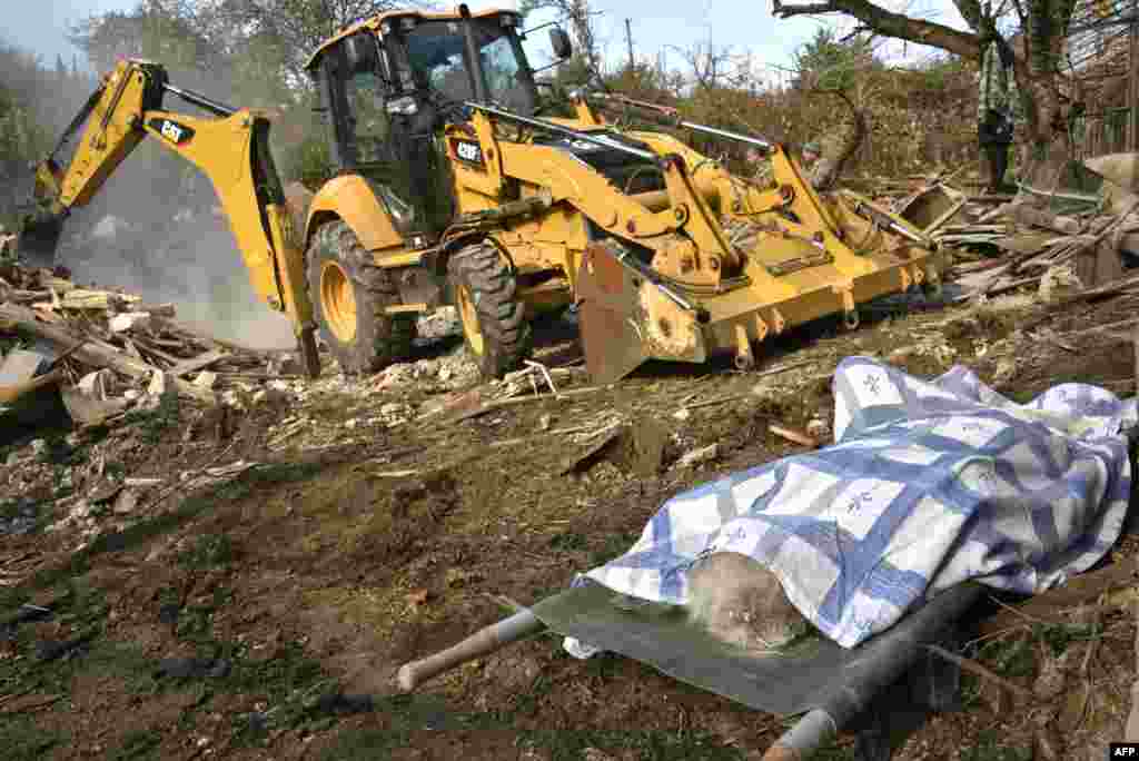 The body of a woman lays on a stretcher near a bulldozer clearing debris of a destroyed house hit by shelling during the military conflict between Armenia and Azerbaijan over Nagorno-Karabakh, in the disputed province's capital of Stepanakert.