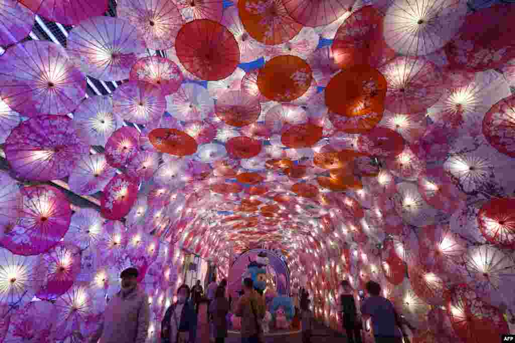 People walk past a display of umbrellas decorated with lights for the upcoming Lantern Festival on a commercial street in Hangzhou, in eastern China's Zhejiang province, Feb. 22, 2021.