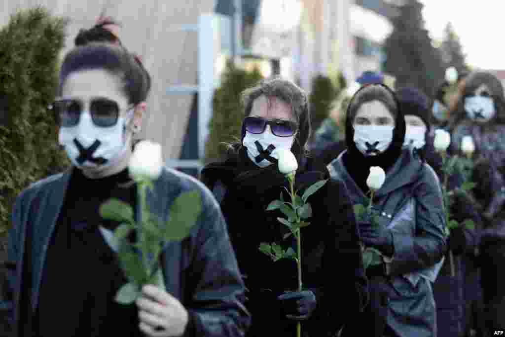 Women in black clothing with their mouths sealed with a tape walk down the street with white roses in Minsk as they protest against the verdict against the Belarusian journalist and doctor who were sentenced to jail for disclosing the medical records of a protester who died after being detained. 