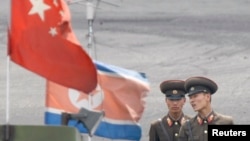 North Korean soldiers chat as they stand guard behind national flags of China (front) and North Korea on a boat anchored along the banks of Yalu River, near the North Korean town of Sinuiju, opposite the Chinese border city of Dandong, June 10, 2013. 