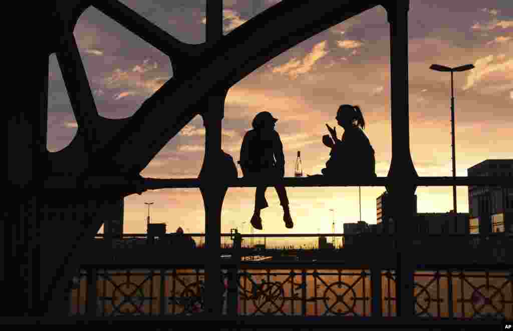 Two women are silhouetted against the setting sun as they sit on a steel beam of a bridge in Munich, southern Germany, April 12, 2018.