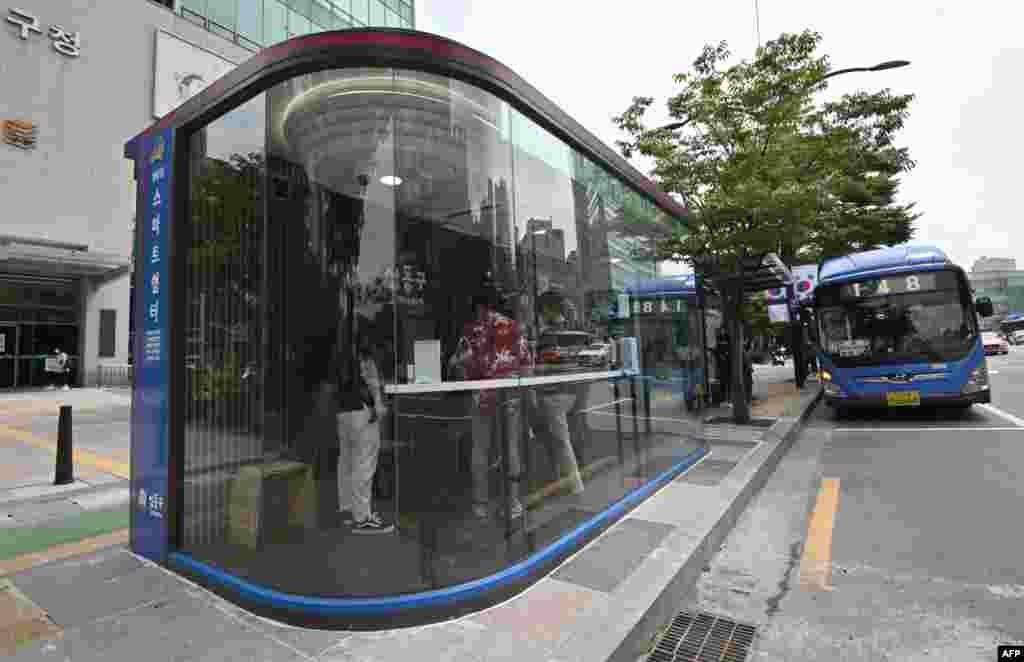 코로나바이러스와 장마, 더위에서 승객들을 보호하기 위해 서울의 한 버스 정류장에 설치된 '스마트안전부스' 안에서 승객들이 버스를 기다리고 있다. 승객은 부스 안으로 들어가기 전에 체온을 측정해야 하고, 여름에는 에어컨이 가동된다.