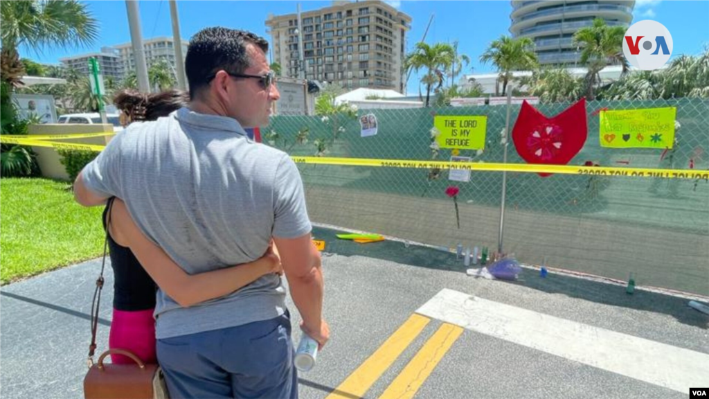Una pareja observa los mensajes de apoyo en la cerca que limita el paso al área del edificio colapsado en Miami Beach.