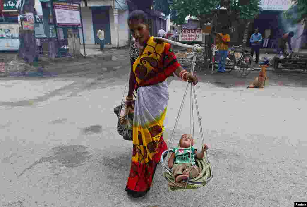 Seorang perempuan memikul bayinya yang tidur di keranjang, di Allahabad, India.