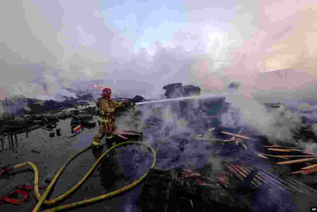 A firefighter battles a fire at a commercial yard in Compton, California. A huge fire visible across Los Angeles burned material in a commercial yard and parked buses.