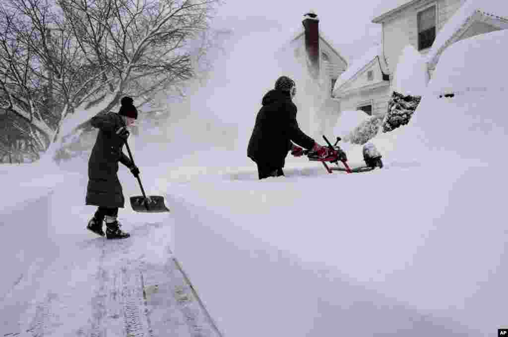 Susan Iannuzzi, left, and Linda Marzell clear a sidewalk after a heavy snowfall on street in Binghamton, New York.