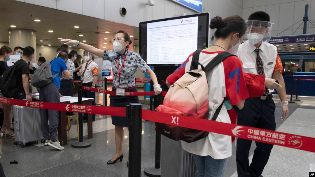 FILE - Airline employees redirect a traveler at a checkpoint for passengers from high-risk areas to present their COVID-19 test results before checking in for their flight at the Beijing Capital Airport terminal 2 in Beijing on Wednesday, June 17, 2020.