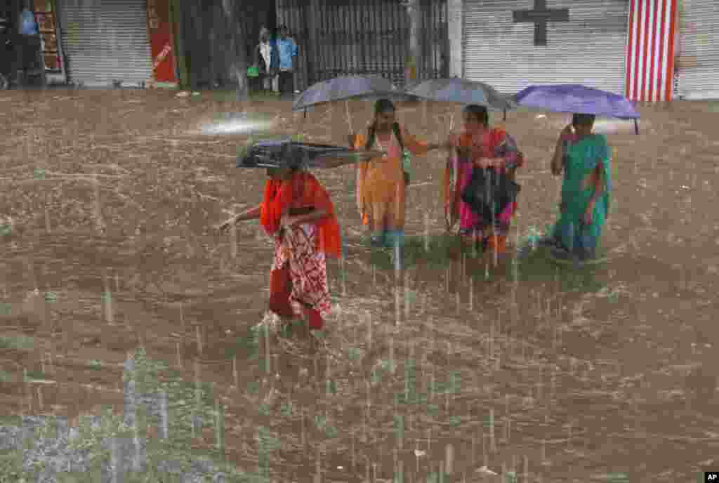 Kaum wanita mengangkat payung dan melangkahi jalan-jalan yang terendam air selama turun hujan di Hyderabad, India. Musim penghujan di India berawal di bulan Juni dan berakhir di bulan Oktober.
