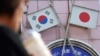 FILE - A woman walks past an advertisement featuring Japanese and South Korean flags at a shop in the Shin Okubo area in Tokyo, Japan, Aug. 2, 2019.